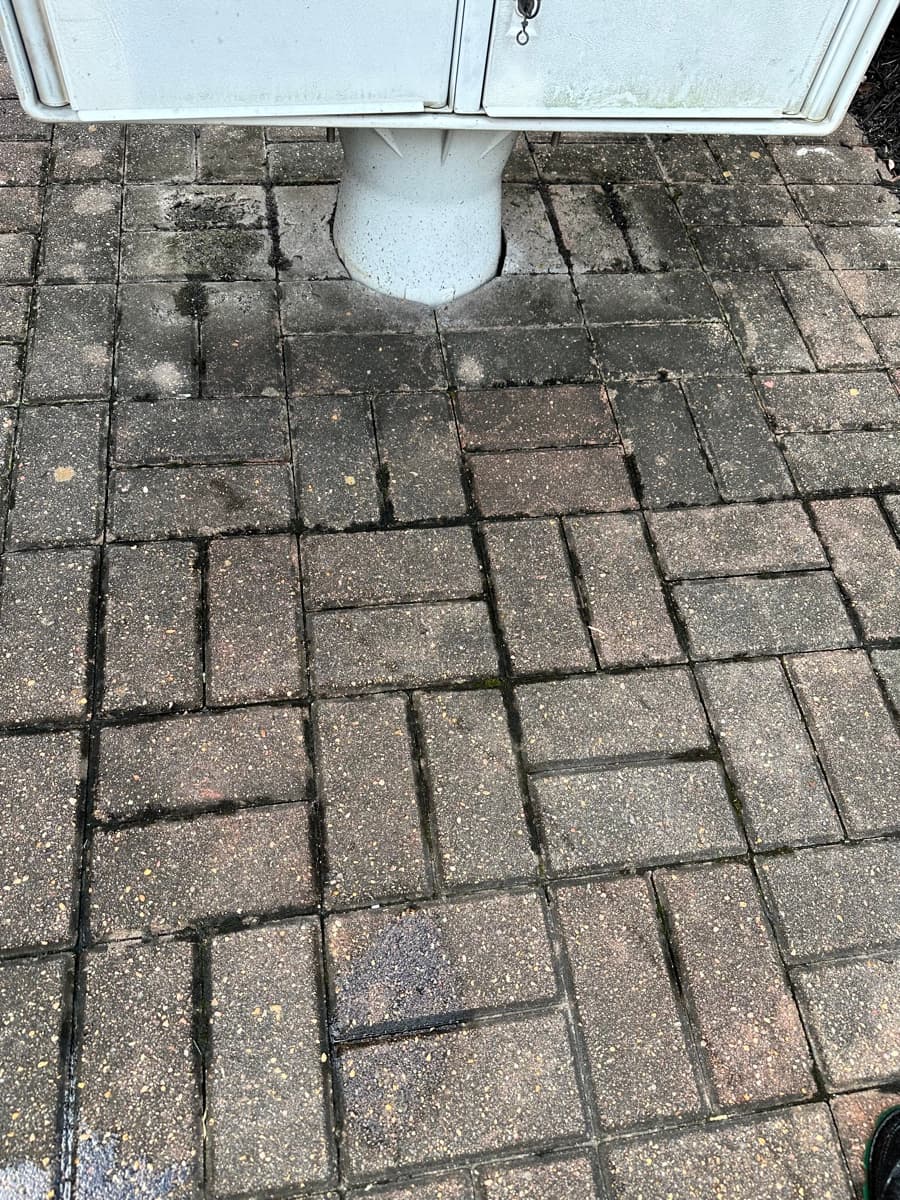 A grimy paver patio before Dhevan pressure-washed it