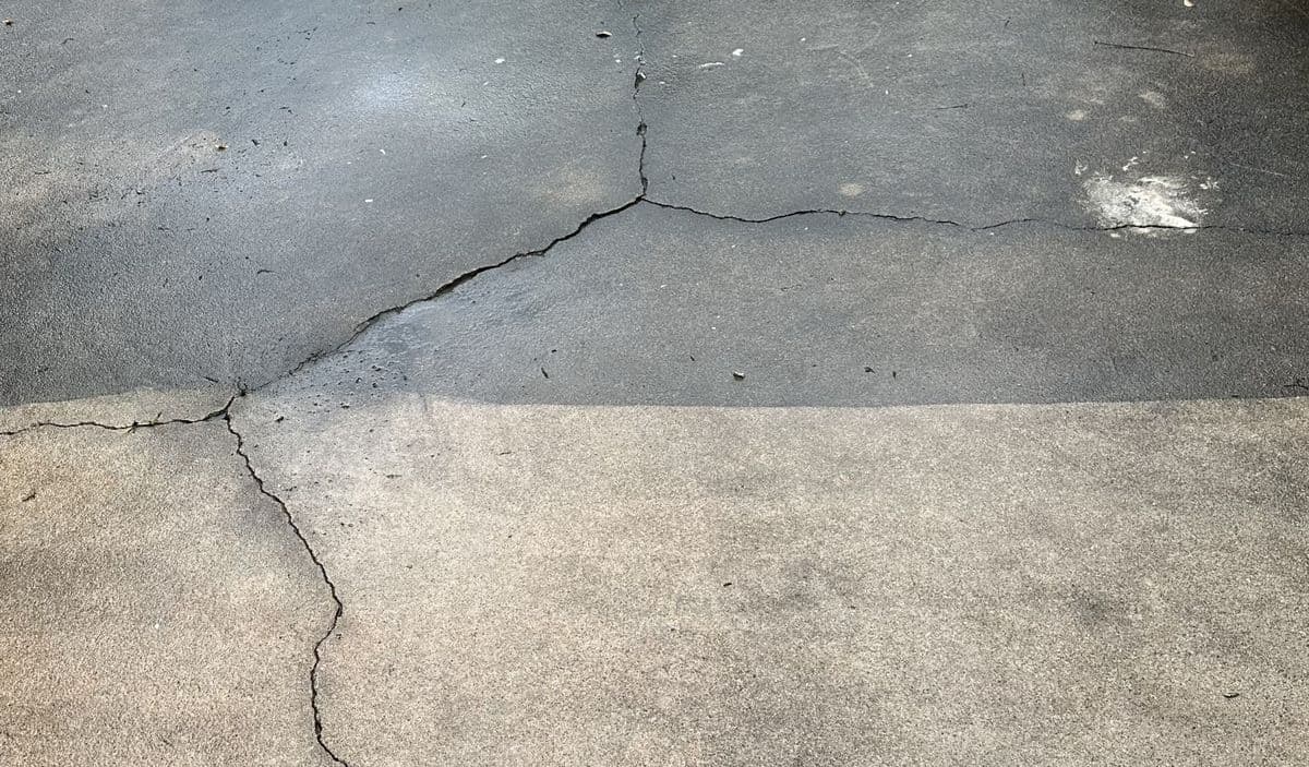 A cracked concrete slab shown before and after cleaning, the washed lower half markedly lighter than the grimy top.